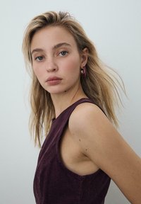 Vinrød ærmeløs top med en struktureret finish og en rundet halsudskæring. Øreringe med øreringe og lilla accenter samt guldfarvet beslag.