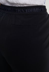 Svarta träningbyxor med ett elastiskt midjeband, utrustade med en bakficka och en slät, lättviktig tyg.