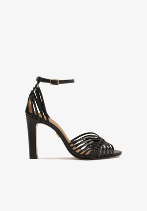 Mustat korkeat sandaalit, joissa on kudottu hihnasuunnittelu, avonaiset varpaat, nilkkaremmillä solki, ja teksturoitu korko. Sileä pinta ja elegantti siluetti.
