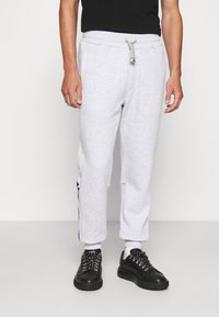 Ljusgrå sweatpants med elastisk midja, dragsko, sidostripes och muddade anklar, tillsammans med svarta sneakers.