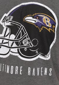 Harmaa t-paita, jossa on Baltimore Ravens -jalkapallokypäräkuva, jossa on valkoisia, violetin ja keltaisia korostuksia. Alla teksti "BALTIMORE RAVENS."