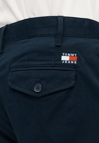 Σκούρο μπλε παντελόνι ναυτικού στιλ με τσέπη που κλείνει με κουμπί και ένα μικρό κεντητό λογότυπο σε κόκκινο, άσπρο και μπλε.