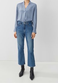 Mönstrad blå blus med v-ringning, långa ärmar och lös passform, kombinerad med högmidjade ljusblå denimculotter och ankelboots.