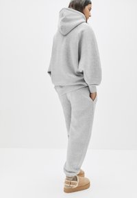 Grauer Baumwoll-Hoodie mit lockerer Passform, kombiniert mit passenden Jogginghosen und beigen Stiefeletten mit Wollakzenten. Schlichtes, nahtloses Design.