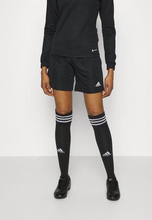 Person wearing black long-sleeve top, black Adidas shorts, black knee-high socks with white stripes, and black athletic shoes standing straight.