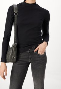 Zwart geribd langärmelig topje met een col, gecombineerd met donkergrijze spijkerbroeken en een grijze schoudertas met een textuur en een metalen riem.