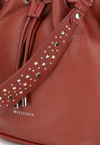 Czerwona skórzana torba w kształcie wiadra z teksturowanym wykończeniem, z wysadzaną ćwiekami rączką z metalowymi ozdobami i srebrnym logotypem.