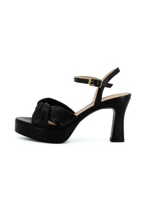 Sandaletto nero con plateau e tacco alto, con cinturino anteriore annodato, cinturino alla caviglia e fibbia dorata su sfondo bianco.