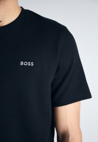 Svart kortermet t-skjorte laget av teksturert stoff, med en liten hvit brodert "BOSS"-logo på venstre bryst.