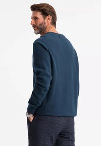 Felpa strutturata di colore blu scuro con maniche lunghe, scollo tondo e vestibilità rilassata; abbinata a pantaloni a scacchi scuri.