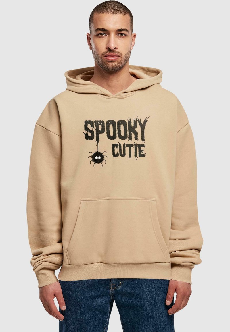 Beige kapuutsi spordija, millel on ees tasku ja must "Spooky Cutie" graafika, millel on koomiksiteemaline ämblik. Pehme puuvillasegune kangas.