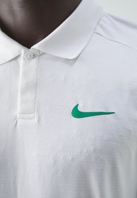 Witte polo met een ademende textuur, voorzien van een groene Nike-logo op de linkerborst en een klassieke kraag met twee knopen.