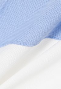 Tissu texturé bleu clair et blanc avec un motif en tricot doux, montrant des transitions en douceur entre les couleurs et une texture bien visible.
