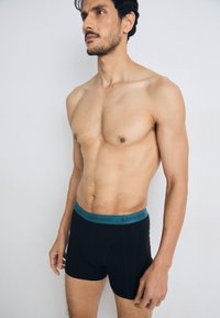 Black boxer briefs with a teal waistband displaying "BJÖRN BORG" logo, featuring a fitted design and soft texture for comfort.