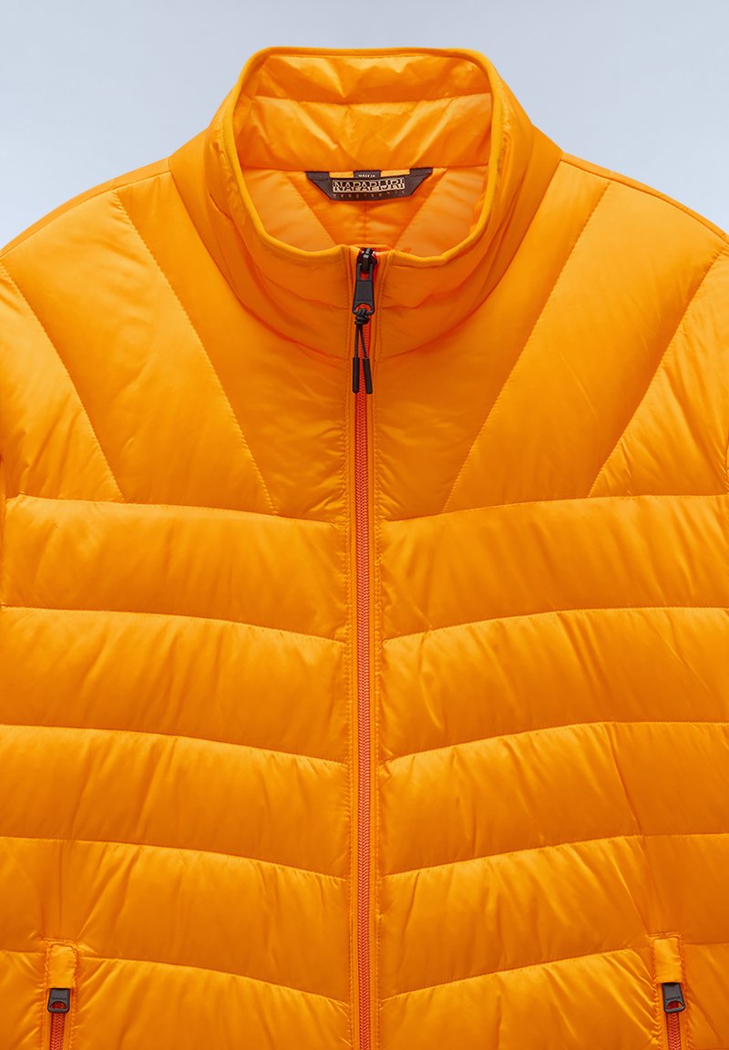 Pomarańczowa kurtka puchowa z pikowanym wzorem, wysoki kołnierz i pełny zamek błyskawiczny. Posiada dwie boczne kieszenie oraz kontrastowe zamki jako detal.