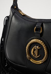 Borsa a tracolla in pelle nera con hardware tono oro, caratterizzata da un emblema decorativo intrecciato e una finitura testurizzata. Include dettagli con frange lungo il lato.