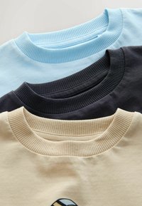 Three crewneck t-shirts in light blue, black, and beige. Visible ribbed collars and smooth fabric texture.