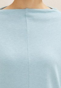 Vaaleansininen neulepaita, jossa on veneehtävä kaula-aukko ja minimalistinen muotoilu. Sileä pinta, jossa on keskiommellus selkäpuolella.