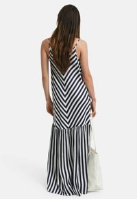 Maxikleid mit marineblauen und weißen Zickzackstreifen, verstellbaren Spaghettiträgern und einem ausgeweiteten, plissierten Saum. Begleitet von einer cremefarbenen Tasche.