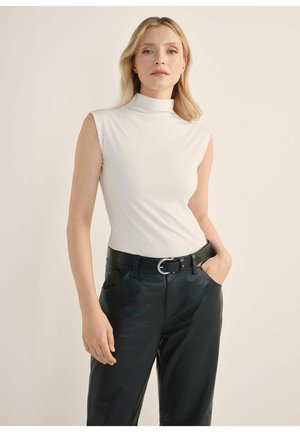 Biały bezrękawnik z golfem w połączeniu z czarnymi skórzanymi spodniami i czarnym paskiem z okrągłą srebrną klamrą. Gładka faktura.