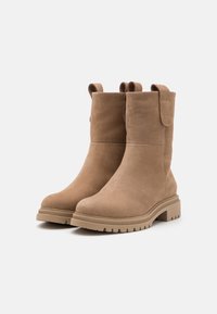 Bottines en cuir brun clair avec une texture lisse, bouts arrondis et tirants en haut. Dotées d'une semelle en caoutchouc robuste et à motifs pour une bonne adhérence.