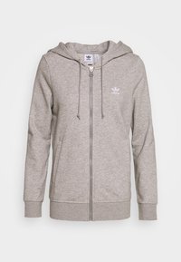 Sweat à capuche gris zippé en matière douce avec capuche à cordon de serrage et poches avant. Il présente un petit logo blanc sur la poitrine gauche.