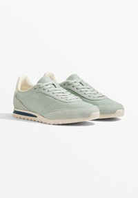 Hellgrüne Sneaker aus einer Mischung aus Wildleder und glattem Leder, mit einem cremefarbenen Innenfutter und einer beigen Sohle mit dunkelblauen Akzenten.