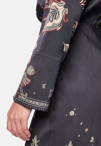 Schwarzer Seidenmantel mit aufwändigen Blumenmustern in Rot und Creme. Verfügt über eine glatte Textur und breite Ärmel mit einer dekorativen Borte.