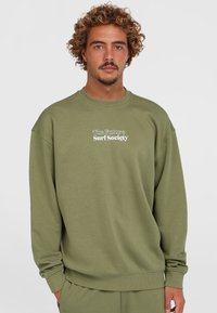 Oliven grøn sweatshirt lavet af en blanding af bomuldsstof. Har en afslappet pasform, ribbet rund hals og et grafisk motiv af "The Future Surf Society" i hvid.