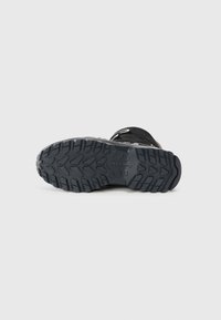 Zwarte wandelschoen zool met een robuust, gestructureerd patroon voor grip. Versterkte randen en een logo-imprint zijn zichtbaar op het rubbermateriaal.