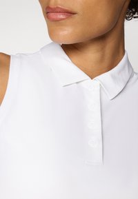 Zbliżenie osoby noszącej białą koszulkę polo bez rękawów z czterema guzikami i ostrym kołnierzem.