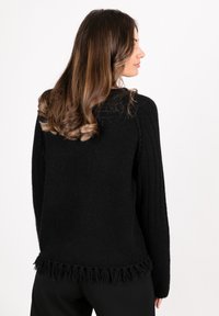 Black knit sweater with ribbed texture, fringe detailing at the bottom, and long sleeves. Background is plain white. No additional features visible.