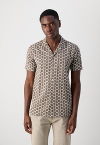 Camisa de mangas curtas em tecido castanho com um padrão geométrico em colmeia na cor creme, com gola em V e botão na frente.