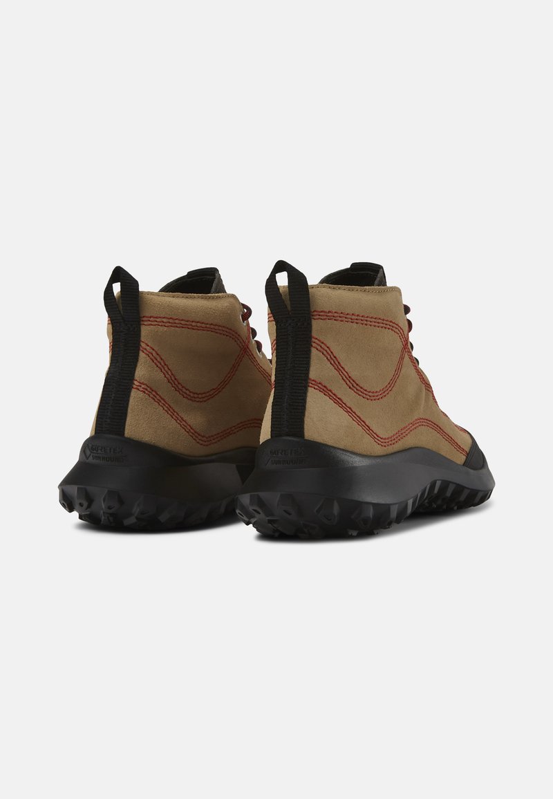 Stivali in suede marrone con suole in gomma nera, caratterizzati da cuciture rosse e un colletto imbottito. Il design include un tassello per una facile calzata.