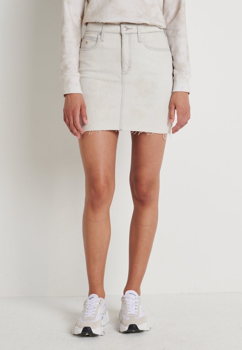 Light gray denim mini skirt with frayed hem, front pockets, and a fitted design, paired with white sneakers. Smooth texture.