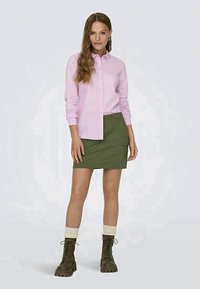 Camisa a rayas rosa claro con botones, falda cargo verde con bolsillo lateral y botas hasta la rodilla color tostado con cordones y suelas gruesas.