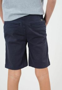 Shorts en coton bleu marine avec deux poches arrière, des coutures décoratives et un écusson logo. Texture lisse avec une coupe droite.