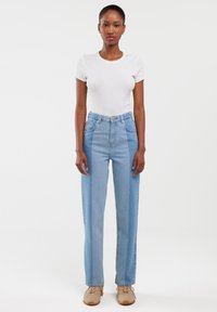 Hoge taille lichtblauwe jeans met een rechte pijpdesign, voorzien van een knoopsluiting en subtiele verticale panelen in verschillende tinten.