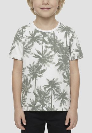 Enfant portant un t-shirt blanc avec un motif de palmier gris et un pantalon noir, debout devant un fond clair uni.