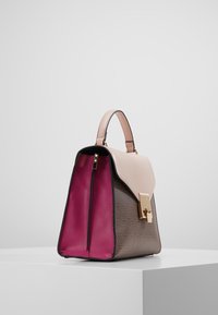 Ustrukturyzowana torebka z różowym uchwytem, beżowym klapem, brązowym wzorzystym korpusem, złotym zapięciem i otwartymi, fuksjowymi wnętrzami na białej powierzchni.