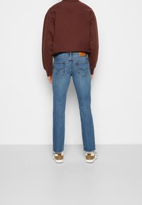 Blå denimjeans med rak passform, medelhögt midjeband och en lapp på bakfickan. Kombinerat med en brun kortärmad sweatshirt och vita sneakers.