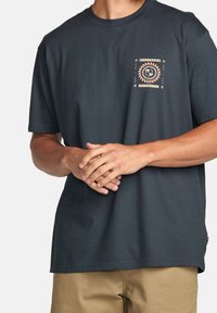 T-shirt en coton gris foncé avec un petit imprimé crème sur la poitrine gauche, manches courtes et col rond.