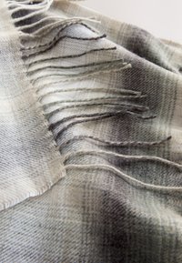 Wool plaid scarf in muted greys and whites, featuring fringed edges and a soft texture, showcasing a checked pattern with varying densities.