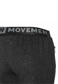 Närbild av svarta, texturerade träningsshorts med en svart midja där det står "MOVEMEN" i grått och en dragkedjeficka på sidan.