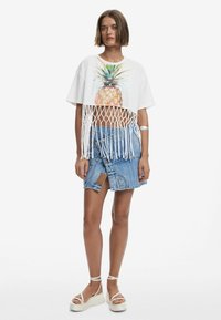 Biele skrátené tričko s potlačou ananásu a strapcami. Modrá denimmová sukňa s vreckami. Biele platformové sandále s členkovými remienkami.
