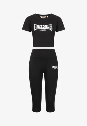 Musta kaksiosainen urheiluasu, joka koostuu lyhythihaisesta crop-topista ja korkeavyötäröisistä capri-leggingseistä, joissa molemmissa on valkoiset "Lonsdale London" -logot.