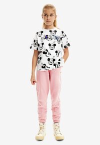 Camiseta blanca con estampados de Mickey Mouse en negro y texto colorido "MINNIE". Pantalones de chándal rosa con costuras laterales, combinados con zapatillas altas blancas.