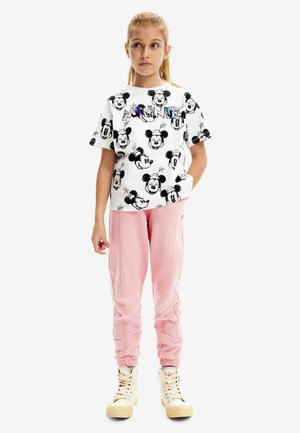 T-shirt blanc avec des imprimés noirs de Mickey Mouse et un texte coloré "MINNIE". Pantalons de survêtement roses avec des coutures latérales, assortis à des baskets montantes blanches.