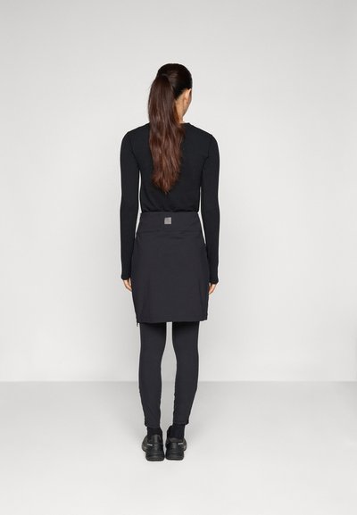 Jupe de sport noire associée à des leggings noirs. La jupe présente une taille haute et une fermeture éclair sur le côté, fabriquée à partir d'un tissu léger et durable.