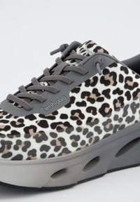 Sneaker à imprimé léopard avec une tige texturée douce en blanc, marron et noir. Elle présente des lacets gris et une semelle épaisse gris avec des découpes.